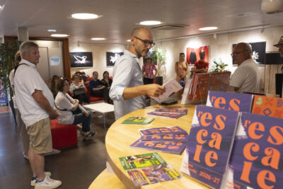 photo dans un hall éclairé, avec au premier plan des programmes où il est écrit "L'Escale", et derrière une dizaine de personnes assises sur des fauteuils - Agrandir l'image 8 sur 13, fenêtre modale