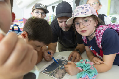 photo d'un groupe d'enfants autour d'une table, vus de près, en train d'étudier un plan pris du ciel avec un animateur - Agrandir l'image 19 sur 21, fenêtre modale