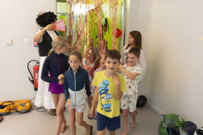 photo d'une dizaine d'enfants dans une salle, qui marchent en rigolant alors qu'ils passent un porte faite de rubans lumineux - Agrandir l'image 12 sur 21, fenêtre modale