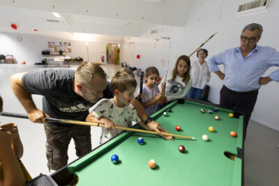 photo d'un groupe d'enfants en train de faire du billard, le Maire et une élue à côté en train de regarder - Agrandir l'image 10 sur 21, fenêtre modale