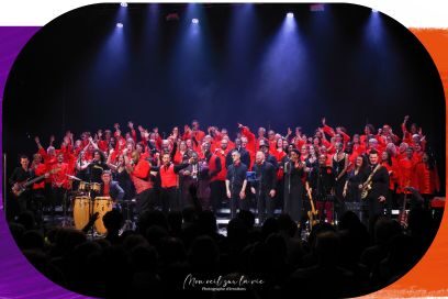 Photo d'ensemble des choristes en toges flamboyantes réunis sur scène sous les rais de lumière bleutés, bras levés vers le ciel pendant leur tour de chant. - Agrandir l'image, fenêtre modale