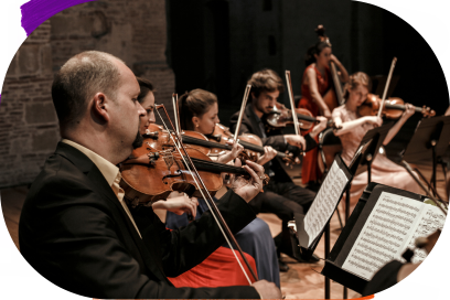 Vue rapprochée de l'arc des violonistes hommes et femmes élégamment vêtus, alignés de profil à la caméra sur uns estrade, devant leurs pupitres dans une belle lumière qui met en valeur le bois des instruments - Agrandir l'image, fenêtre modale