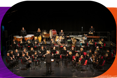 Vue d'ensemble en plongée sur les musiciens de l'orchestre réunis sur scène avec leurs instruments, dans la pénombre de la salle de spectacles sous les lumières des projecteurs, sous la baguette du directeur musical en costume élégant, debout dos au public. - Agrandir l'image, fenêtre modale