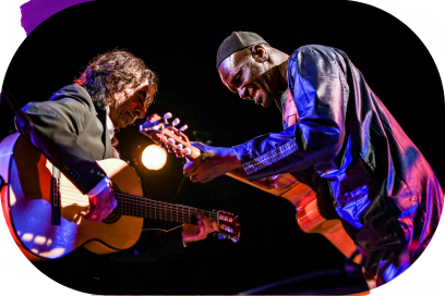 Sur scène l'un tout près de l'autre avec leurs isntruments respectifs et concentrés sur leur musique les deux artistes sourient les yeux baissés dans une attitude mimétique sous les lumières violettes. - Agrandir l'image, fenêtre modale