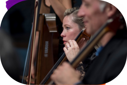 Plan rapproché sur deux musiciens de profil en train de jouer, l'ai concentré de profil à la caméra, une contrebassiste et un violoncelliste, en train de sourire à leur directeur musical hors champ, l'image est floûtée artistiquement autour d'eux. - Agrandir l'image, fenêtre modale