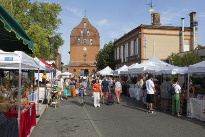 photo paysage d'une rue avec l'église à l'arrière-plan,et sur chaque côté de la rue des stands de commerçants, et des gens qui passent et s'arrêtent - Agrandir l'image 15 sur 15, fenêtre modale