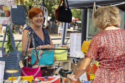 photo d'un stand de vente de sacs, avec une femme derrière qui sourit à l'objectif pendant qu'une autre femme regarde les sacs - Agrandir l'image 14 sur 15, fenêtre modale