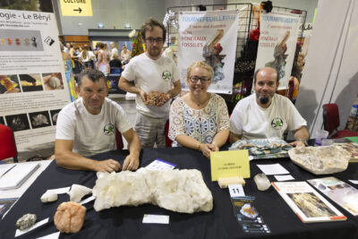 photo de quatre personnes derrière un stand "Le Béryl club de géologie", sur lequel on voit plusieurs grandes pierres. derrière eux, on voit des affiches du salon des minéraux et fossiles - Agrandir l'image 11 sur 16, fenêtre modale