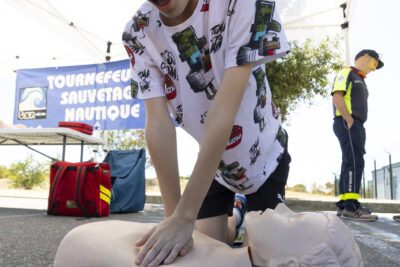 photo d'un jeune garçon qui pratique un massage cardiaque sur un mannequin au sol, en extérieur - Agrandir l'image 11 sur 14, fenêtre modale