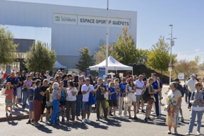 photo de la foule rassemblée devant la scène, sur un parking neutralisé, au soleil, devant l'espace sportif de quéfets, un grand bâtiment - Agrandir l'image 3 sur 14, fenêtre modale
