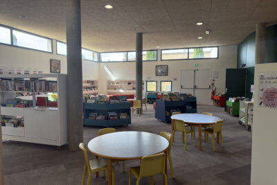 photo de l'intérieur de la Médiathèque, on voit des tables rondes, des étagères avec des livres - Agrandir l'image 5 sur 6, fenêtre modale
