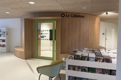 photo d'un espace avec étagères blanches de documents et derrière l'entrée par une porte aux entourages verts vers une salle circulaire - Agrandir l'image 2 sur 3, fenêtre modale