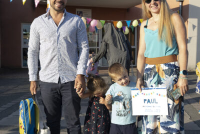 photo d'une famille qui sourit à l'objectif dans la cour d'école, un homme et une femme tiennent par la main deux enfants - Agrandir l'image 18 sur 25, fenêtre modale