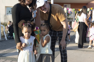 photo d'une famille dans la cour d'école qui pose en souriant, une femme et un homme avec deux enfants un peu timides - Agrandir l'image 17 sur 25, fenêtre modale