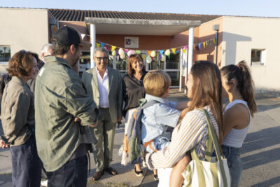 photo du Maire et de l'élue Rachida Lucazeau qui échangent en souriant avec une famille dans une cour d'école ensoleillée - Agrandir l'image 16 sur 25, fenêtre modale