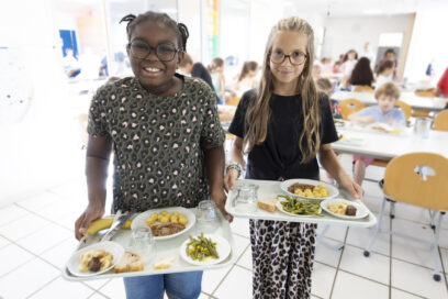 photo paysage de deux jeunes filles qui sourient à l'objectif en tenant leur plateau repas, dans une cantine lumineuse - Agrandir l'image, fenêtre modale