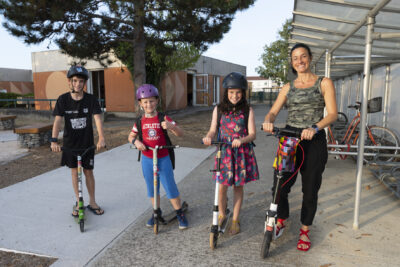 photo d'une femme et trois enfants, tous sur leurs trottinettes qui posent en souriant pour la photo dans une cour d'école - Agrandir l'image 22 sur 25, fenêtre modale