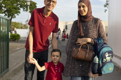 photo d'une famille, un homme et une femme accompagnent leur enfant à l'école, sourire à l'objectif - Agrandir l'image 23 sur 25, fenêtre modale