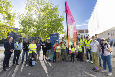photo d'une quinzaine de personnes, adultes et enfants réunis, avec des gilets et des pinces pour attraper les déchets, dehors, sous un temps ensoleillé - Agrandir l'image 1 sur 9, fenêtre modale