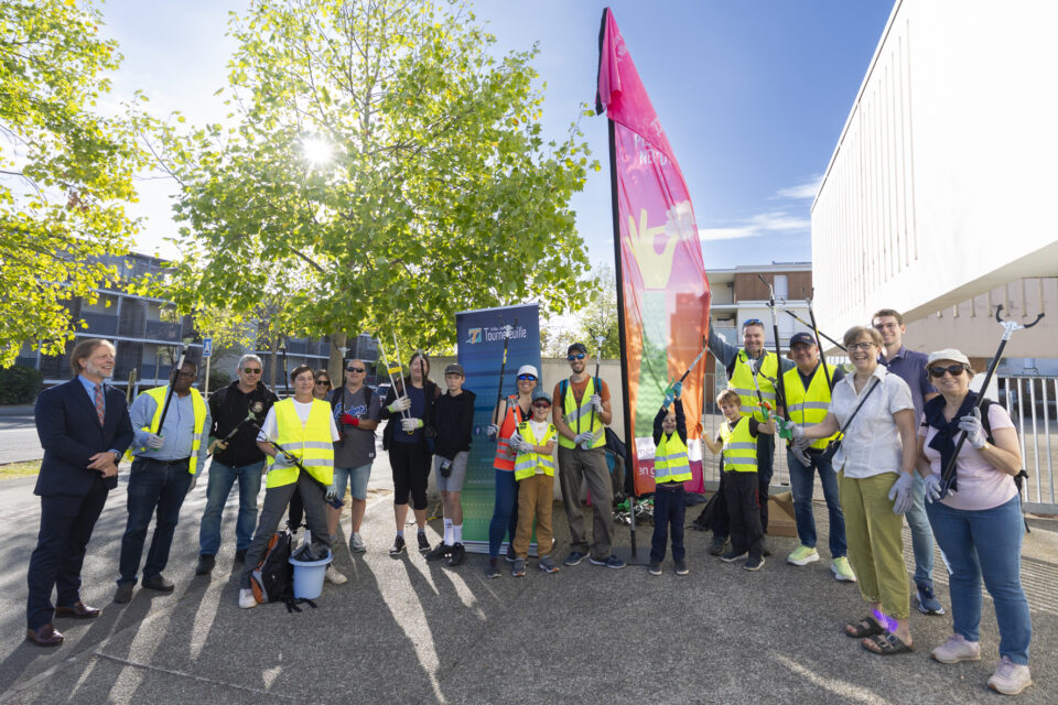 photo d'une quinzaine de personnes, adultes et enfants réunis, avec des gilets et des pinces pour attraper les déchets, dehors, sous un temps ensoleillé