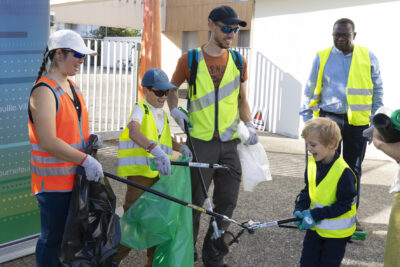 photo d'une famille avec deux enfants, deux adultes, en gilets fluo et avec des pinces pour attraper les déchets, ils tiennent des sacs poubelles - Agrandir l'image 3 sur 9, fenêtre modale