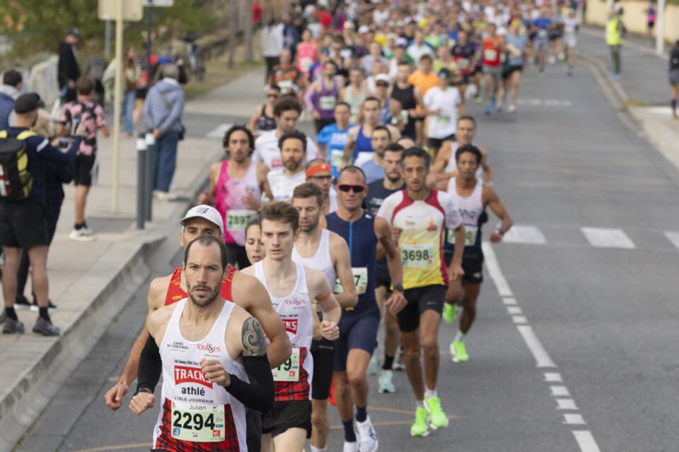 photo de la course sur la rue, devant quelques hommes en tête en plein effort, derrière des centaines de coureurs