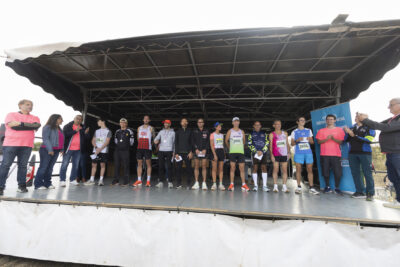 photo paysage d'une scène sur laquelle une dizaine de coureurs sont rassemblés en ligne et applaudis par d'autres personnes habillées de rose - Agrandir l'image 18 sur 19, fenêtre modale