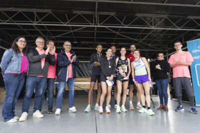 photo paysage avec sur la partie droit six coureurs rassemblés, devant trois femmes et derrière trois hommes, avec médailles et coupes, autour des coureurs six personnes applaudissent, vêtues de rose - Agrandir l'image 17 sur 19, fenêtre modale
