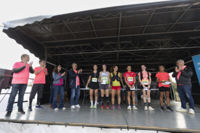 photo paysage d'une scène sur laquelle six coureurs sont rassemblés en ligne et applaudis par cinq autres personnes habillées de rose - Agrandir l'image 19 sur 19, fenêtre modale