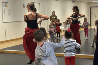 photo d'enfants qui dansent avec une professeur en tenue de flamenco, dans une salle de danse, face à un grand miroir - Agrandir l'image 7 sur 18, fenêtre modale