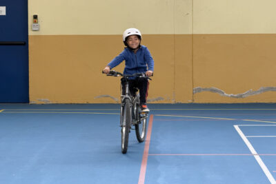 photo d'un enfant en train de faire du vélo dans un gymnase, tout sourire - Agrandir l'image 10 sur 18, fenêtre modale