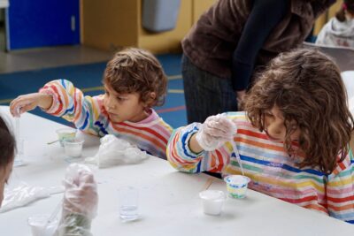 photo de deux enfants concentrés à une table en train de verser quelque chose dans un petit récipient comme des petits chimistes - Agrandir l'image 12 sur 18, fenêtre modale
