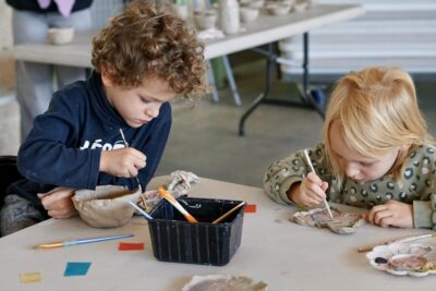 photo de deux enfants assis à une table qui utilisent un pinceau sur un objet de poterie gros - Agrandir l'image 16 sur 18, fenêtre modale