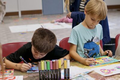 photo de deux enfants assis à une table qui dessinent avec concentration, à l'aide de gros crayons - Agrandir l'image 15 sur 18, fenêtre modale