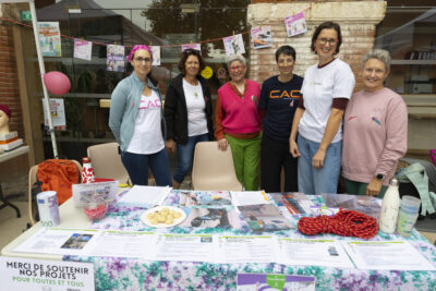 photo d'un stand avec une table et des documents posés dessus, derrière la table six femmes debout sourient à l'objectif - Agrandir l'image 7 sur 16, fenêtre modale