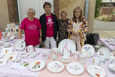 photo d'un stand d'assiettes illustrées, et de mugs, derrière on voit quatre femmes souriantes qui se tiennent debout et sourient à l'objectif - Agrandir l'image 11 sur 16, fenêtre modale