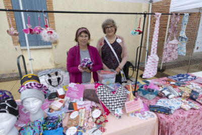 photo d'un stand en extérieur, avec nappes roses et des objets en vente, comme des foulards, bonnets, coussins ou totebag - Agrandir l'image 15 sur 16, fenêtre modale