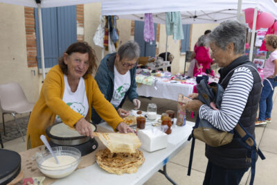 photo d'un stand de crêpes, deux femmes derrière sourient à l'objectif, elles portent un tee-shirt blanc avec un dessin vert et écrit "ça pousse à Pahin" et servent une crêpe à une femme devant elles - Agrandir l'image 4 sur 16, fenêtre modale
