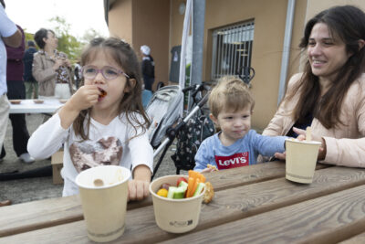 photo d'une famille avec deux enfants en train de grignoter des légumes crus et une femme souriante à côté, tous trois sont assis à une table en bois - Agrandir l'image 8 sur 11, fenêtre modale