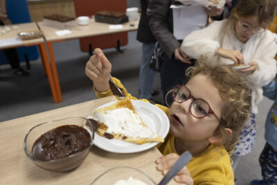 photo d'une jeune fille qui met de la mousse au chocolat sur une crêpe pliée en triangle dans une assiette - Agrandir l'image 5 sur 11, fenêtre modale