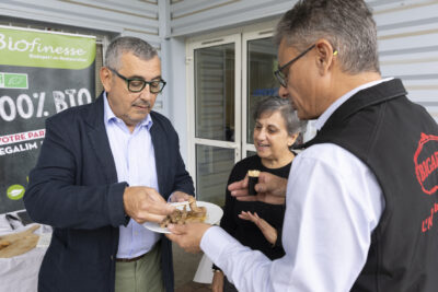 photo du Maire qui prend un morceau type émincé dans une assiette en carton tenue par un producteur - Agrandir l'image 3 sur 11, fenêtre modale