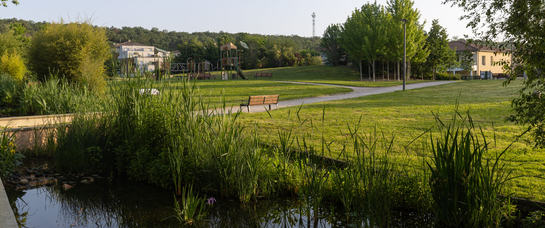 Photo de parc avec aire de jeux au fond et cours d'eau au premier plan