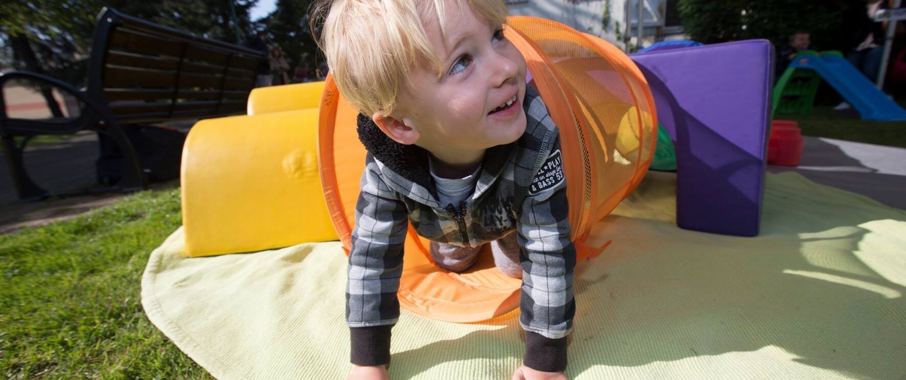 Enfant blond qui sort d'un jeu à quatre pattes, en extérieur