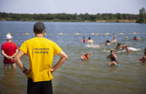 Photo de lac avec des gens qui se baignent devant un sauveteur aquatique