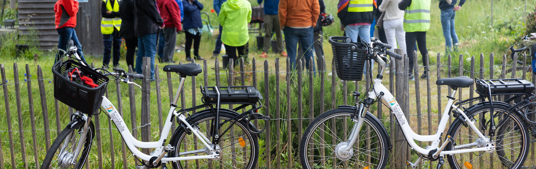 Photo de deux vélos floqués ville de tournefeuille au premier plan et d'un groupe de personnes derrière dans un jardin