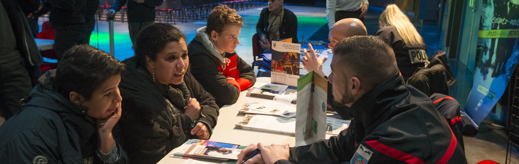 Jeunes accompagnés de parents qui discutent avec des adultes à un stand d'information