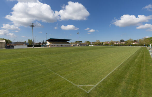Photo du terrain de foot avec tribune au fond, depuis point de corner