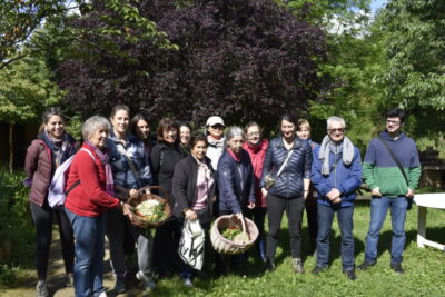 Photo d'un groupe de personnes rassemblées à l'extérieur dans un environnement naturel, elles portent des paniers et sourient à l'objectif - Agrandir l'image 1 sur 1, fenêtre modale