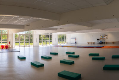 Photo d'une salle de gymnastique vide, sur la gauche une baie vitrée, au sol, des steps - Agrandir l'image 4 sur 8, fenêtre modale