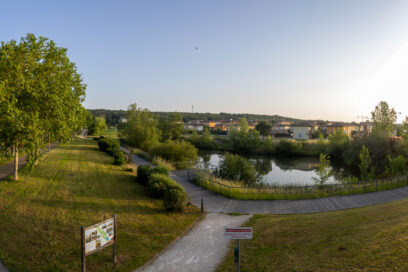 Photo panorama du parc de la Paderne, chemin piétonnier qui se sépare à gauche et droite et derrière, un cours d'eau. On aperçoit des habitations à l'arrière-plan - Agrandir l'image, fenêtre modale